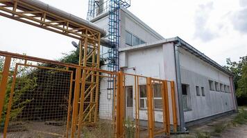 Abandoned industrial building with rusting metal fence and overgrown weeds, symbolizing urban decay and economic decline photo