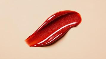 Amber toned lip gloss smear with hints of red shimmer isolated on a soft muted cream background photo