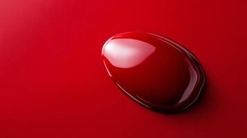Closeup of ruby red nail polish drop with thick texture glossy finish reflecting light against a smooth background photo