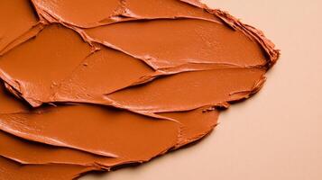 Closeup of terracotta clay mask smeared in rough organic lines on a smooth beige background photo