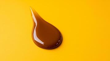 Glossy caramel lip gloss in a thick luminous droplet with highlights catching warm light on a creamy background photo