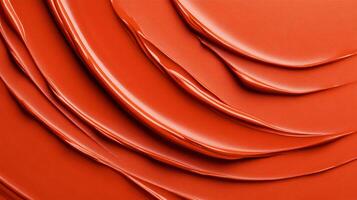 Swirls of rich coppery red liquid lipstick creating an abstract pattern on a soft muted orange background photo