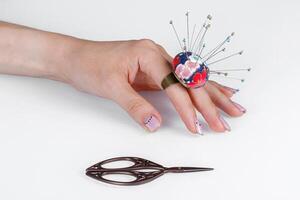 a ring with a small pillow for needles on a hand and scissors on a white background photo