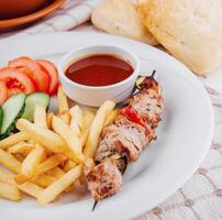 Grilled pork skewer with french fries and tomato sauce served on a plate photo