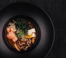 Steaming miso soup with salmon and shiitake mushrooms in black bowl photo