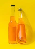 Two bottles of orange juice with blank labels leaning on a yellow background photo