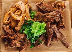 Grilled meat assortment with lettuce on craft paper lying on wooden board photo