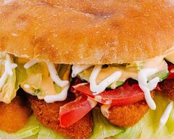 Delicious crispy chicken burger with fresh vegetables and sauce is lying on a white surface photo
