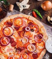 Delicious pizza lying on wooden table with ingredients spread around photo
