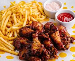 Crispy chicken wings and fries with dips on table photo