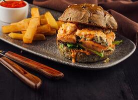 Delicious salmon burger with blue cheese and fries served on gray plate photo
