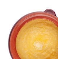 Steaming polenta with melting butter in clay pot on white background photo