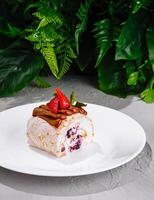 Meringue roll decorated with strawberries and chocolate ganache on white plate photo