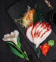 Sliced octopus sashimi with wasabi and ginger on slate serving board photo
