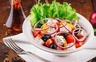 Greek salad with feta cheese, vegetables and olives on rustic wooden table background photo