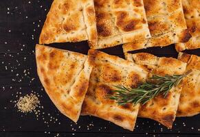 Turkish ramadan pide bread on dark wooden table with sesame and rosemary photo