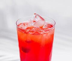 Red cocktail standing on white cube with palm leaf shadow photo