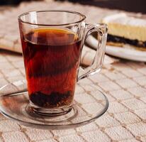 Steaming glass of black tea resting on tablecloth with cake in background photo