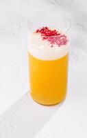 Refreshing yellow cocktail with white foam and raspberry powder topping on white background photo