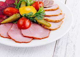 Plate combining several types of meat cuts and pickles being served on white table photo