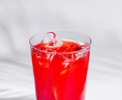 Refreshing red cocktail standing on white cube with tropical palm leaf shadow photo