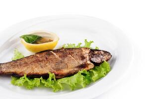 Grilled trout served on bed of lettuce with lemon and condiment photo