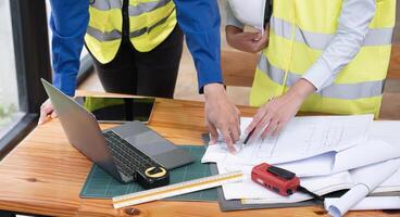Young Engineers Collaborate on Construction Plans with Blueprints and Digital Tools in Modern Office Setting photo