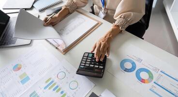 Close-Up of Accountant Performing Financial Calculations with Charts, Graphs, and Calculator on Desk in Modern Office photo