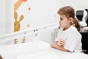 A little girl enjoys an engaging vision game on state-of-the-art ophthalmic equipment. The Rainbow system enhances eyesight in a comfortable and welcoming environment. photo