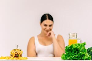 Young, full-figured woman faced with the choice between healthy food and unhealthy options. Perfect for promoting detox, dieting, and weight loss, highlighting the decision for a healthier lifestyle photo