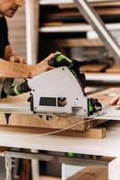 Unrecognizable man working with professional, electric circular saw, making a precise cut along the guide on a wooden surface. Tool is connected to a dust extraction system. Woodworking workshop. photo