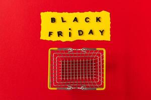 Black friday basket. Top view of yellow torn paper sheet and black friday text on red background. With shopping cart. photo
