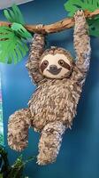 delightful sloth with textured fur made from layers of paper clings to a branch, surrounded by green leaves, set against a light blue background. photo