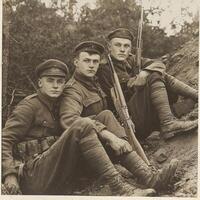 Three soldiers sit together each holding a rifle displaying camaraderie and bravery. They are dressed in period uniforms set against a natural backdrop typical of World War I. photo