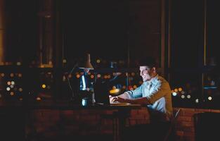 Joyful Man Working On Laptop Computer Browsing Internet Sitting Late At Night In Modern Office. Empty Space For Text photo