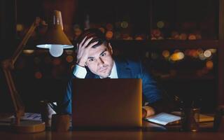 Serious Entrepreneur Man At Laptop Thinking On Business Idea Overnight Sitting In Modern Office. Low Light photo