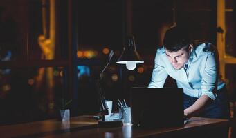 Hardworking Employee. Busy Businessman Working On Laptop Standing In Modern Office Late At Night. Free Space photo