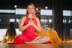 Meditation and concentration. a woman in a red dress, sitting on the floor with her eyes closed, is practicing medicine indoors. Peace and relaxation photo