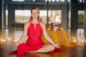 Meditation and concentration. a woman in a red dress, sitting on the floor with her eyes closed, is practicing medicine indoors. Peace and relaxation photo