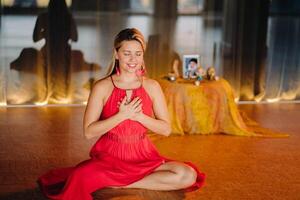 Meditation and concentration. a woman in a red dress, sitting on the floor with her eyes closed, is practicing medicine indoors. Peace and relaxation photo