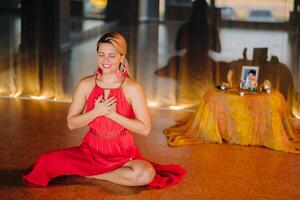 Meditation and concentration. a woman in a red dress, sitting on the floor with her eyes closed, is practicing medicine indoors. Peace and relaxation photo