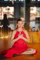 Meditation and concentration. a woman in a red dress, sitting on the floor with her eyes closed, is practicing medicine indoors. Peace and relaxation photo