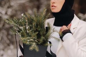 A girl in a white suit and balaclava with a package of Christmas trees in the winter forest on New Year's Eve.New Year's concept photo