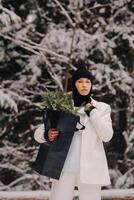 A girl in a white suit and balaclava with a package of Christmas trees in the winter forest on New Year's Eve.New Year's concept photo
