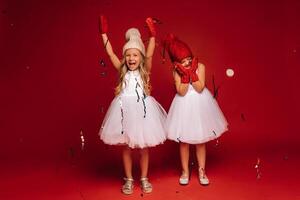 two little girls in white dresses hats and mittens sprinkle confetti on a red background photo