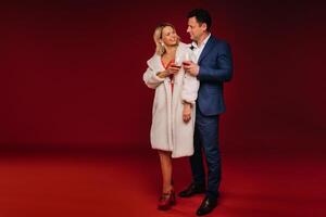 A man and a woman in love with a glass of champagne on a red background embrace photo