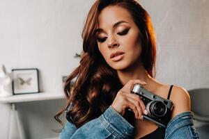 a brunette with long hair poses in a studio sitting on a chair with a camera in her hands photo