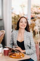 A girl sits in a cafe and looks at a tablet, a Girl in a coffee shop smiles, Distant work photo