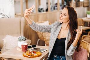 a business Girl is sitting in a cafe and taking a selfie,a Girl in a coffee shop is smiling and taking a selfie on a smartphone photo