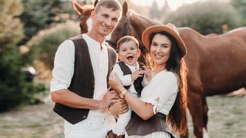 A family in white clothes with their son stand near two beautiful horses in nature. A stylish couple with a child are photographed with horses photo